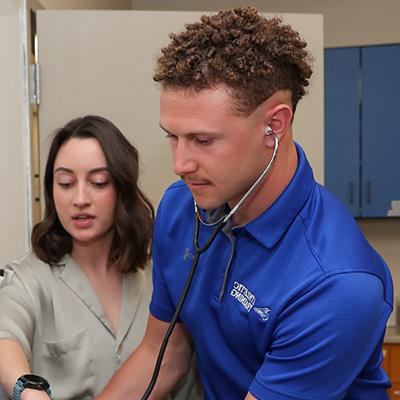 a student and instructor work with a dummy (offscreen) in a clinical setting 